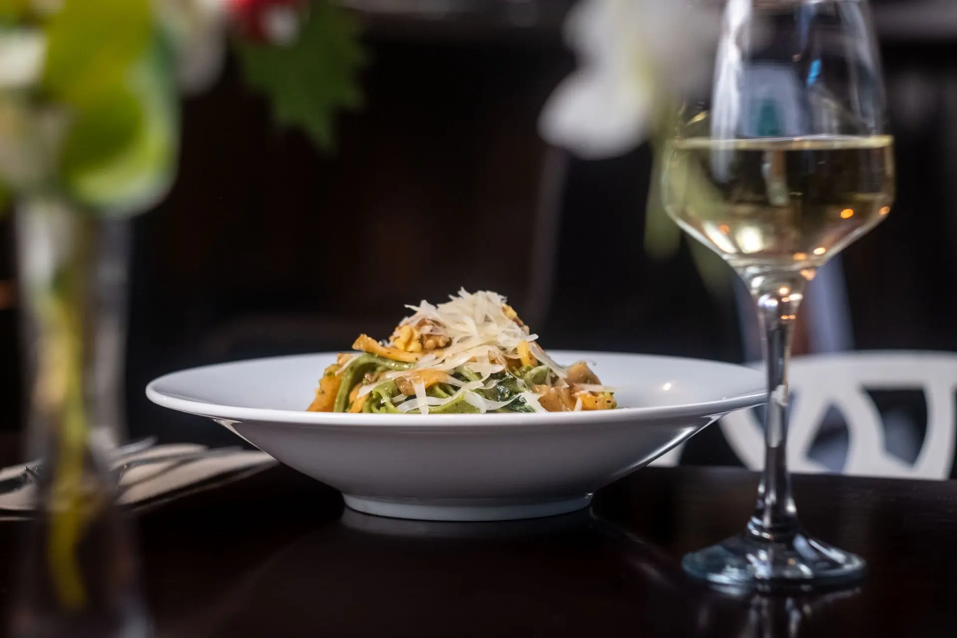 Plato de pasta con queso rallado y copa de vino blanco, fotografía de alta cocina para restaurante en Barcelona