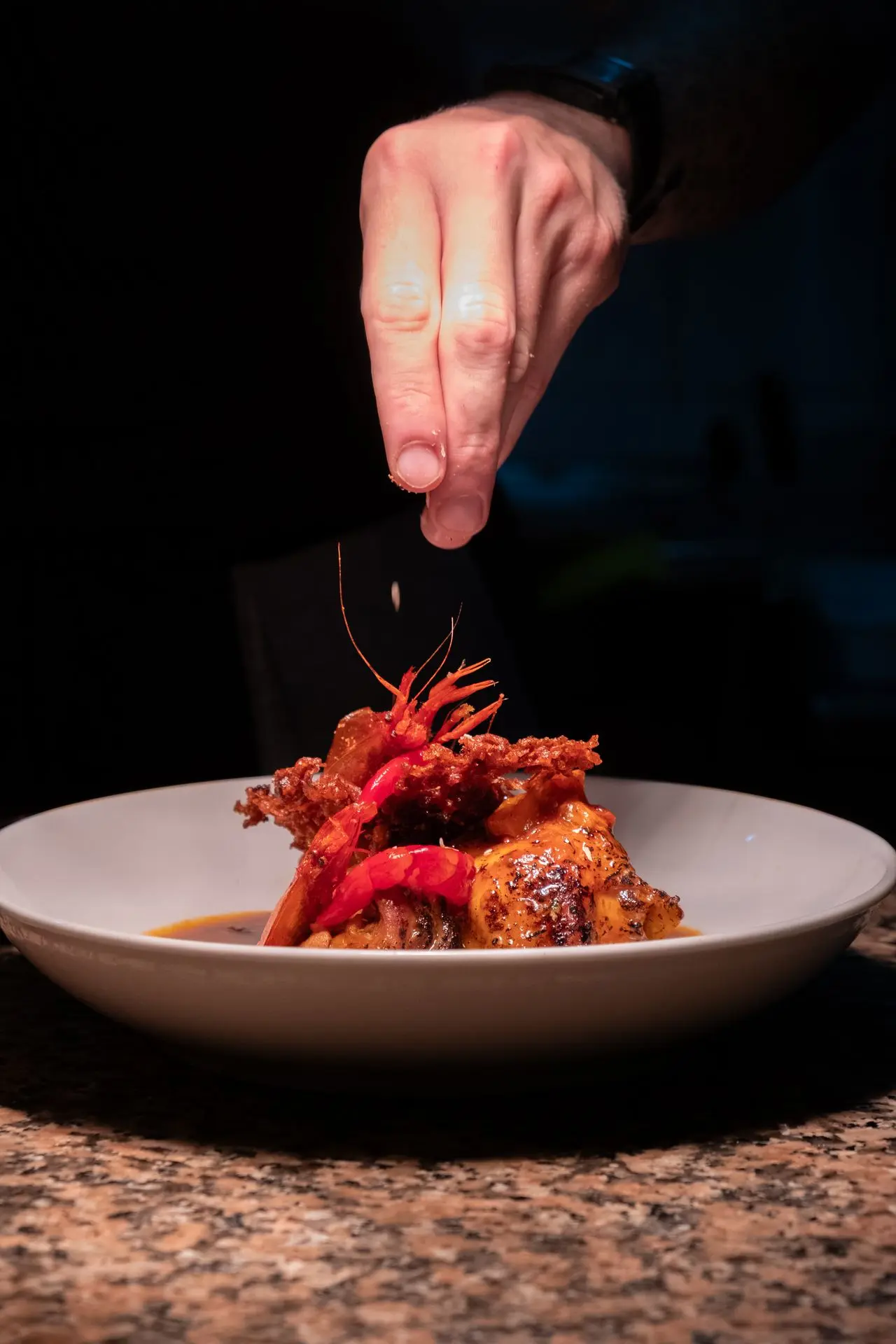 Chef emplatando plato gourmet de marisco con toque final, fotografía culinaria profesional en Barcelona