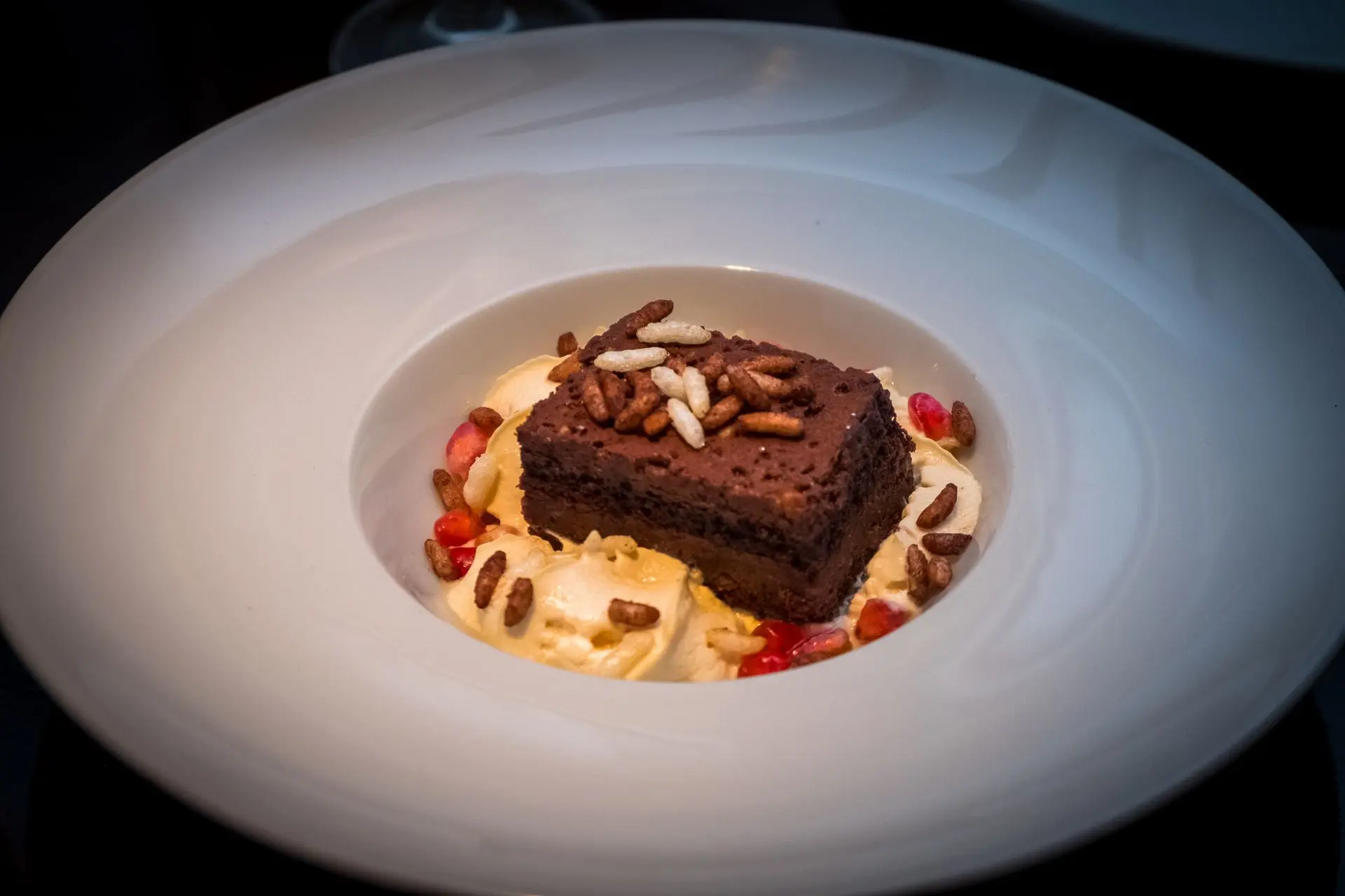 Postre de brownie de chocolate con helado, frutos rojos y piñones, alta repostería para restaurante en Barcelona