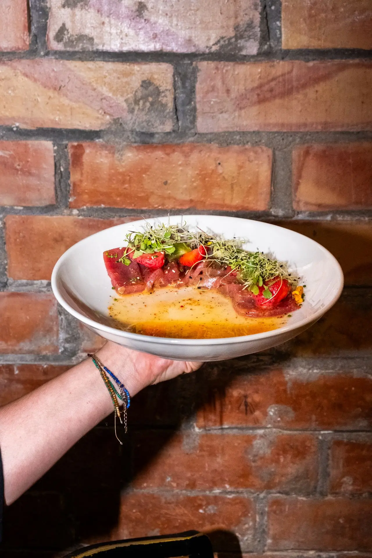 Mano sosteniendo plato de tataki de atún rojo, con brotes y salsa, fotografía de cocina fusión en Barcelona